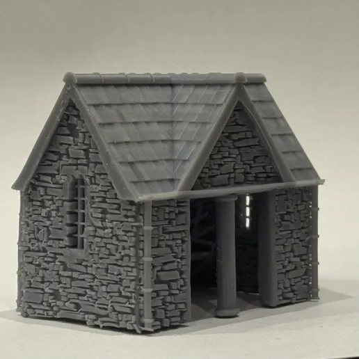 Angled view of the printed bus stop showing the stone side wall with a narrow window, slate roof and open front.