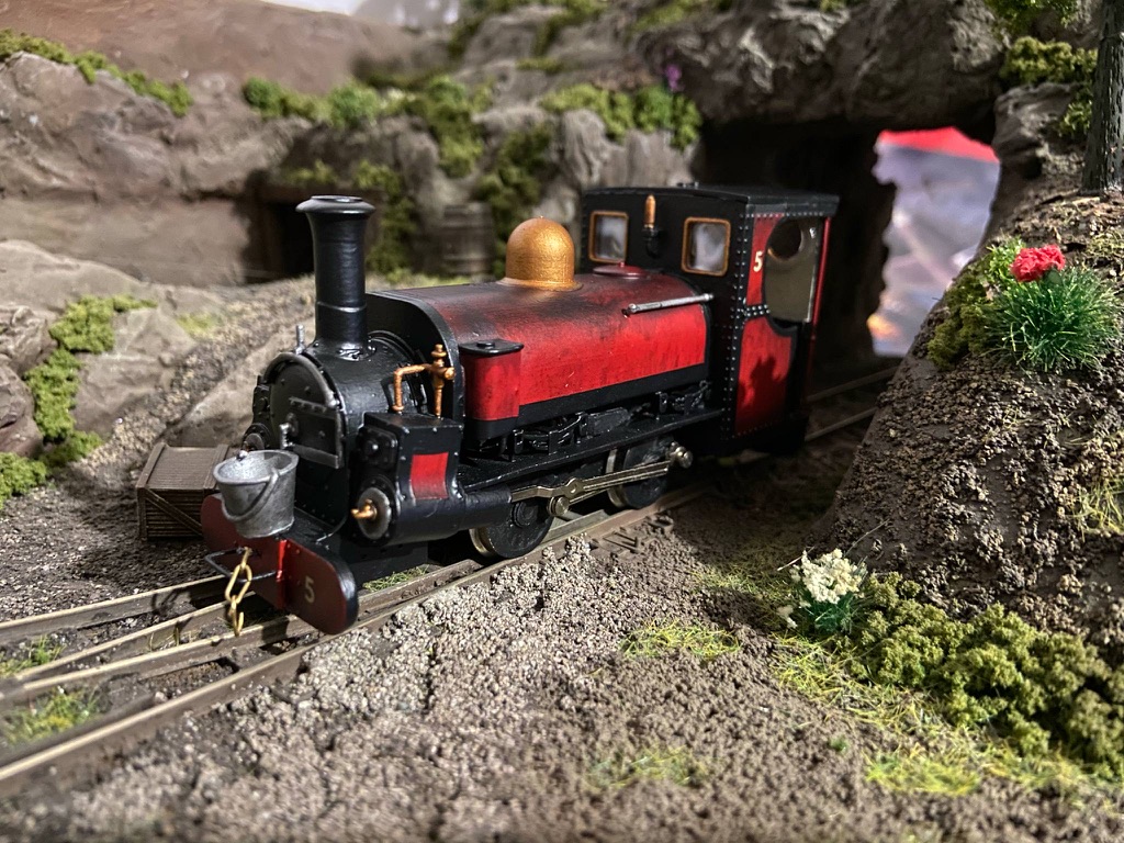 Charles painted in red and black with a brass dome and number 5, running on a narrow gauge layout beside a rock cutting.