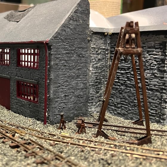 Painted hoist standing over the shed road beside a stone workshop, with axle jacks on the ballast.