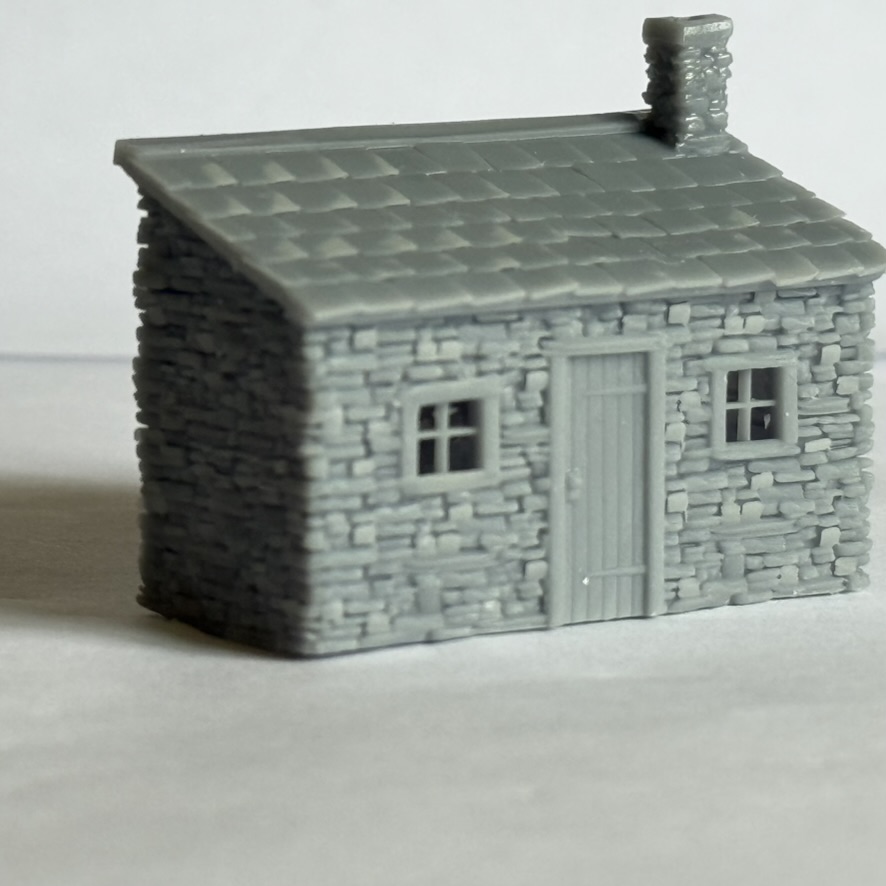 Three-quarter front view of the printed stone lineside hut showing the slate roof, chimney, door and window details.