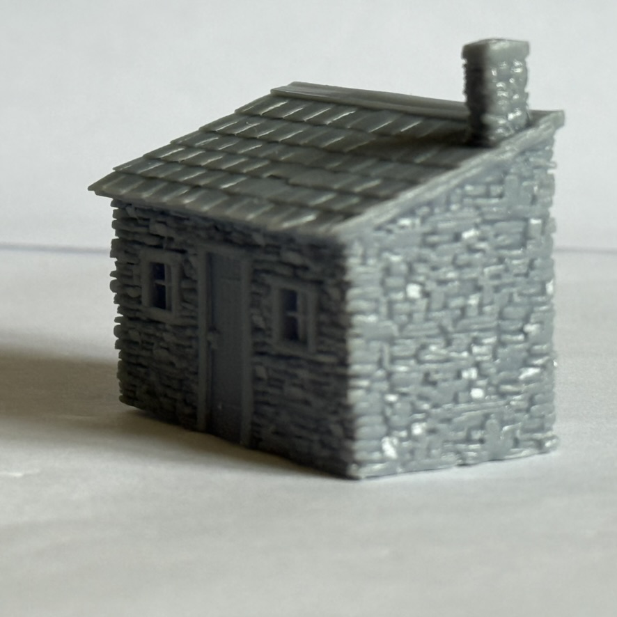 Angled side and front view of the printed stone lineside hut showing the wall texture, door, windows and chimney.