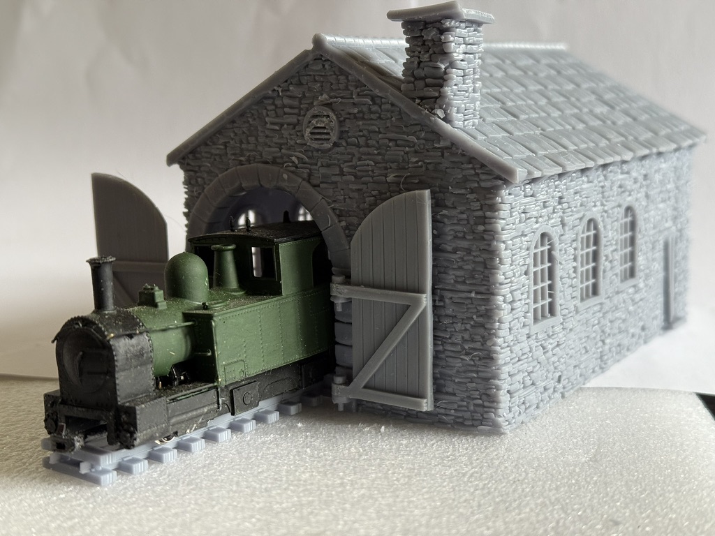 Three-quarter view of the 009 slate loco shed with a narrow gauge locomotive coming out of the arched entrance