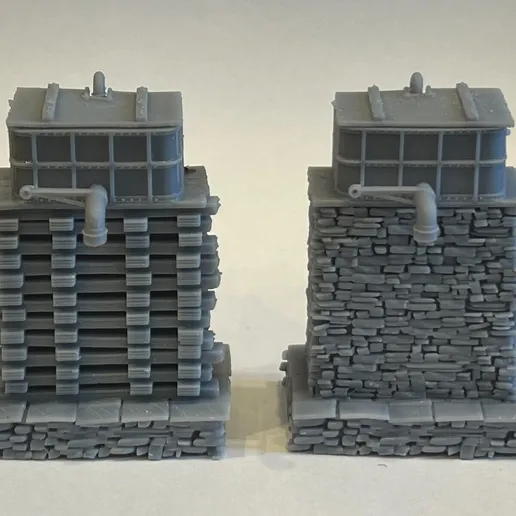 Two printed narrow gauge water towers side by side, one on a stacked sleeper base and one on a stone base, each topped with a panelled tank and filler pipe.