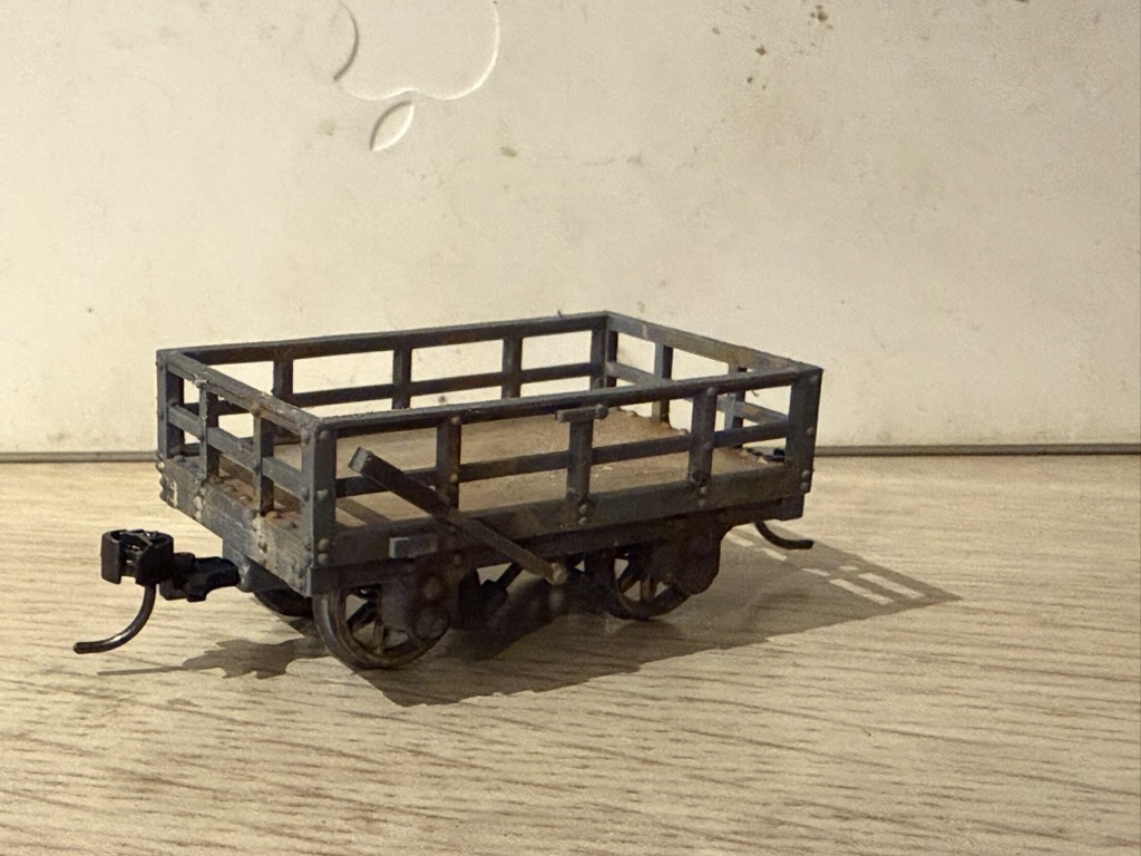 Weathered grey printed open wagon with railed sides, brake lever and plank floor, fitted with a coupling at one end.