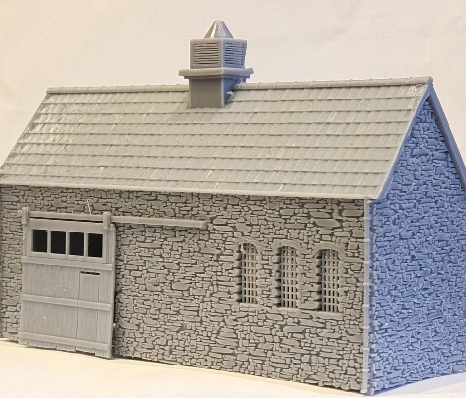 Three-quarter view of the printed single storey stone workshop with a slate roof, louvred ridge ventilator, sliding door and three arched windows.