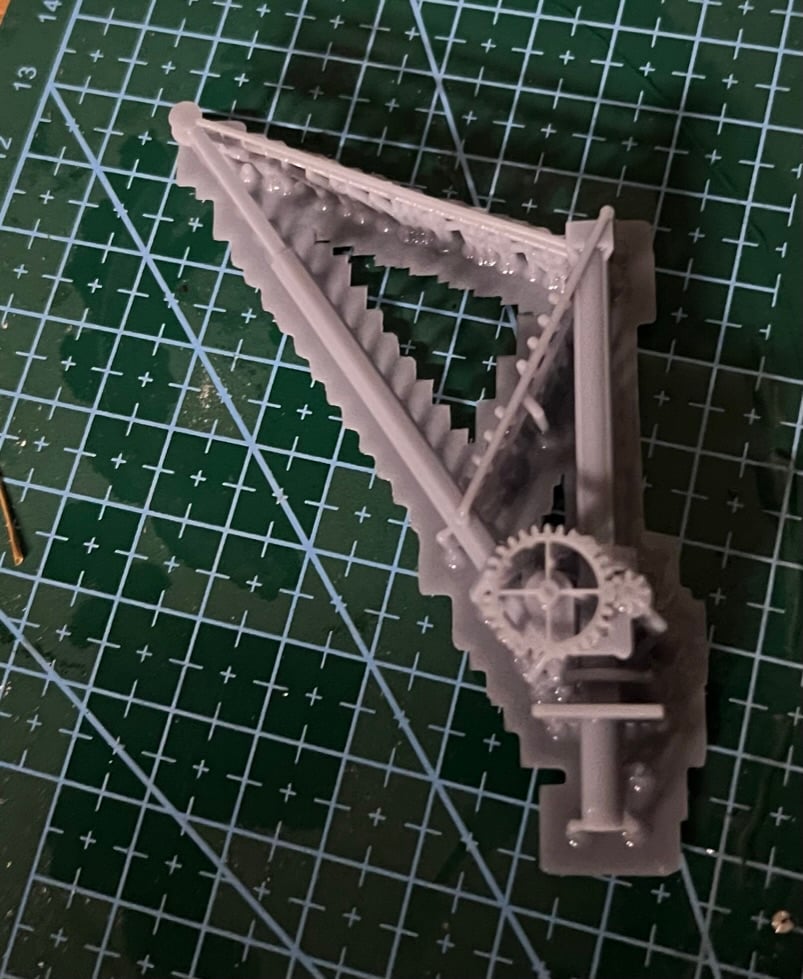 Freshly printed small crane lying on a cutting mat with its print supports still attached beneath the jib and gears.