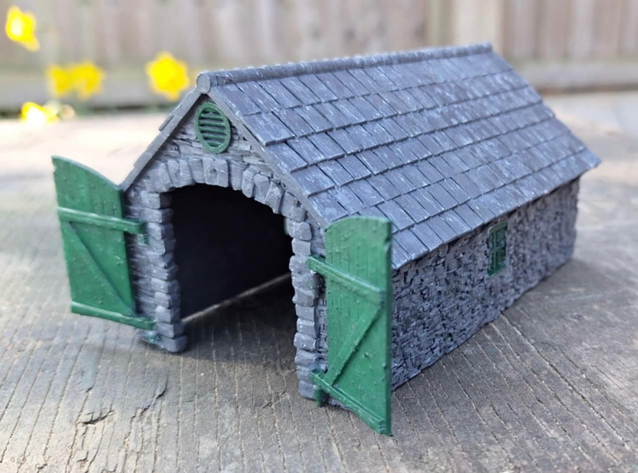 Painted smaller 009 stone loco shed with green doors open beneath the arched entrance