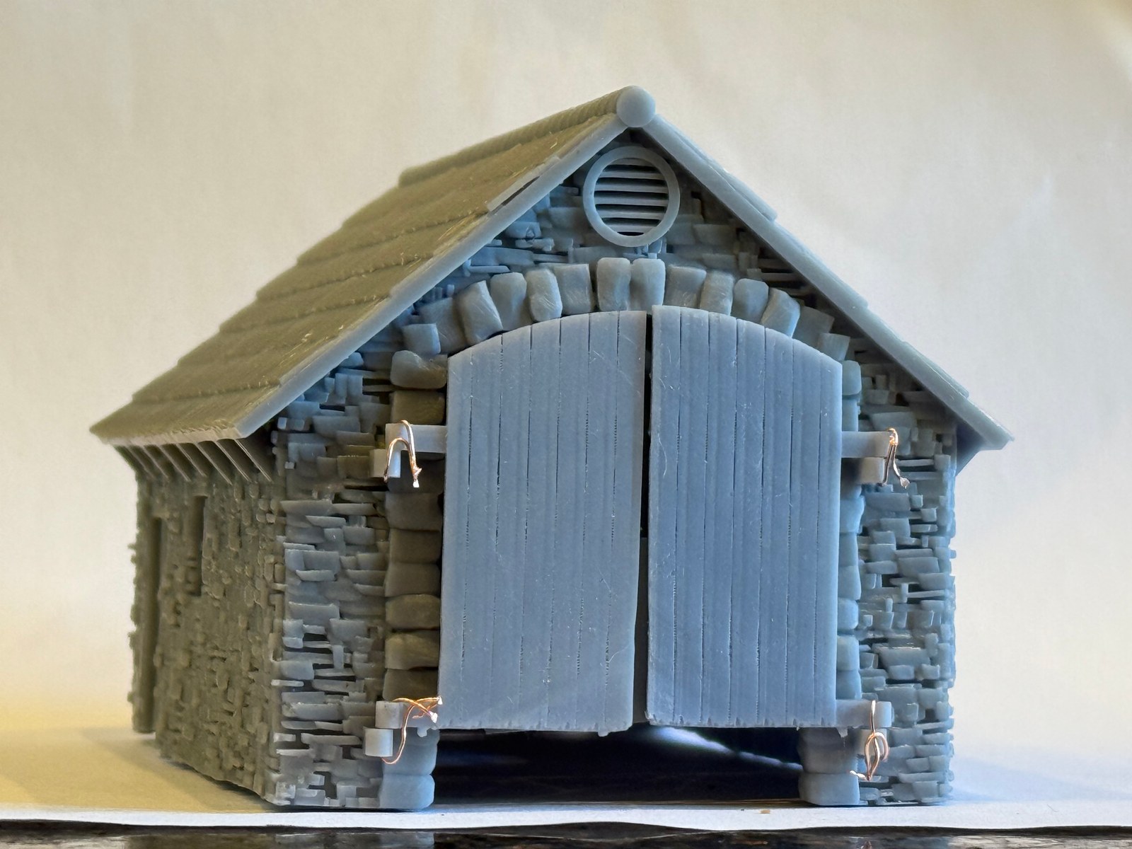 Unpainted smaller loco shed with both plank doors closed beneath the round gable ventilator